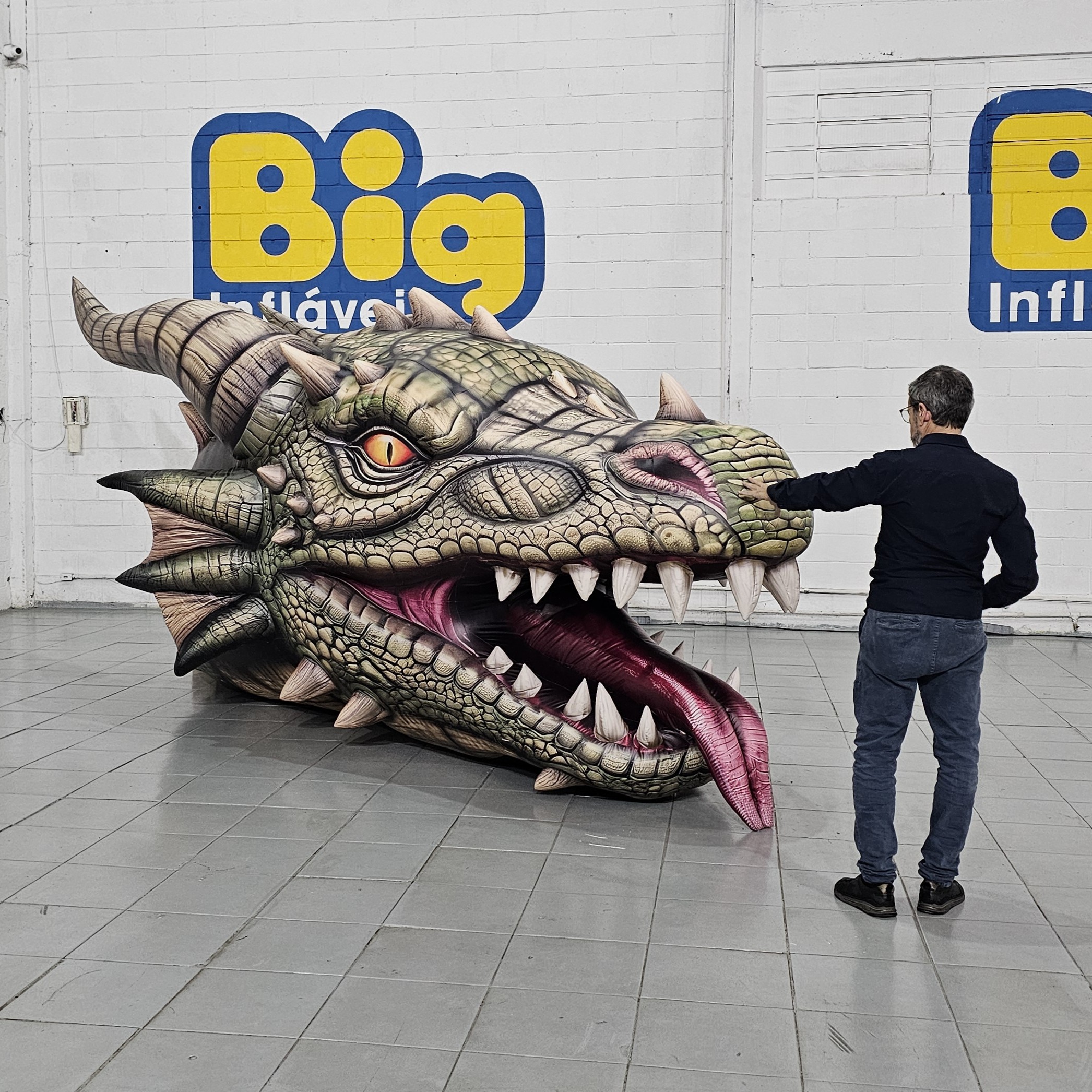 Cabeça de dragão inflável finalizada ao lado de uma pessoa, mostrando sua escala monumental